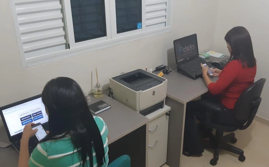 Duas pessoas trabalhando em notebooks em mesas encostadas na parede de um cômodo de casa, o primeiro escritório da Co.Crie