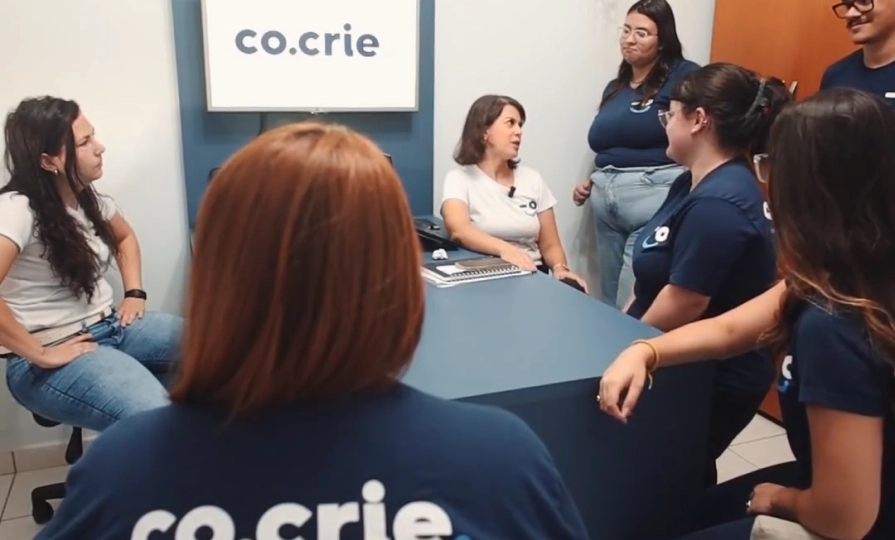 Equipe da Co.Crie reunida em volta da mesa durante uma conversa, a maioria de camiseta da agência